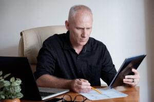 Homem de meia-idade analisando documentos e usando um tablet em seu escritório.