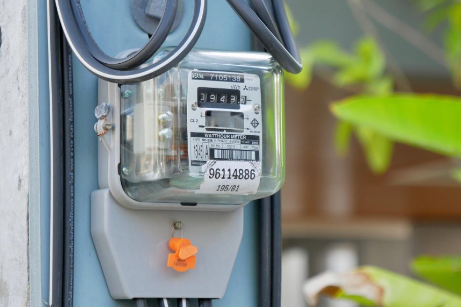 medidor de luz Medidor de energia elétrica instalado em um poste, com fios conectados e vegetação ao fundo.