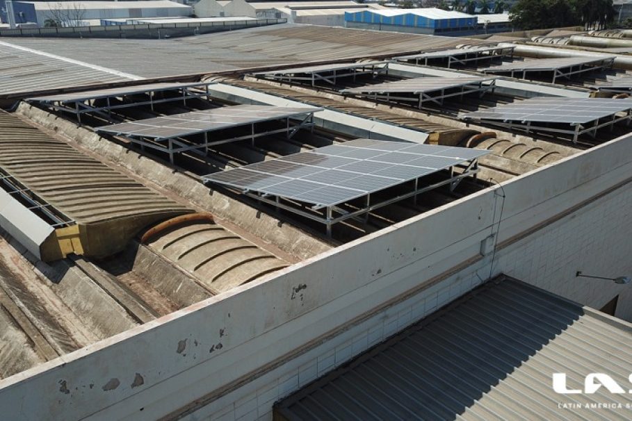 Painéis solares instalados sobre um telhado industrial com estrutura metálica elevada. A marca LAS (Latin America Solar) está visível no canto inferior direito da imagem.