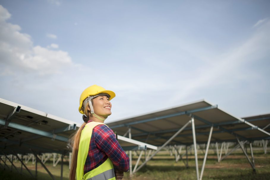 Engineer electric woman checking and maintenance of solar cells. Engenheira sorrindo com capacete de segurança amarelo em usina de energia solar.