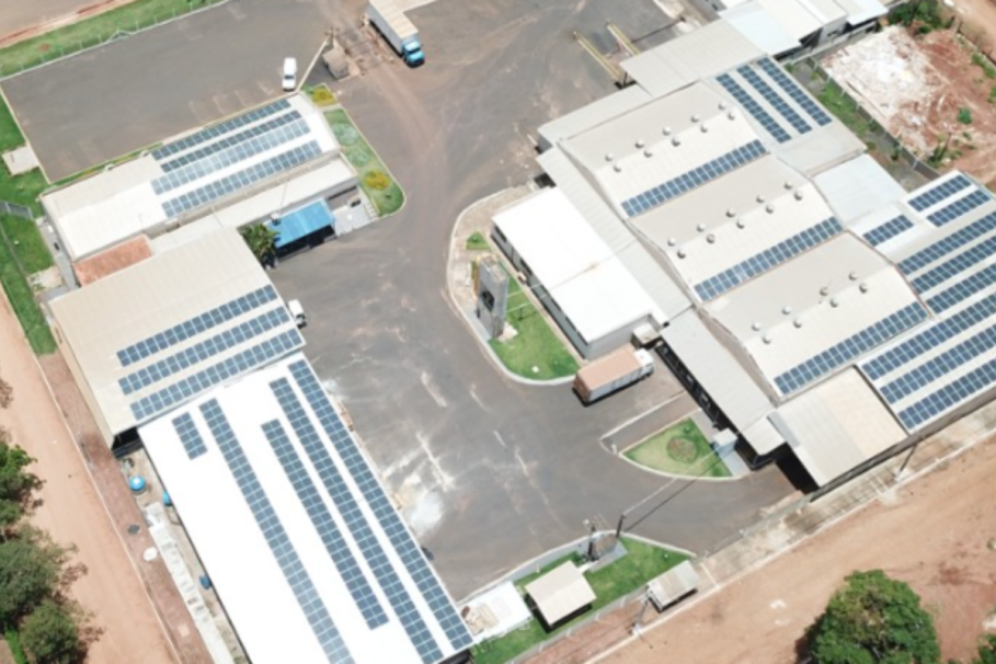 Vista aérea de um complexo industrial com telhados equipados com painéis solares, destacando o uso de energia limpa e sustentável.